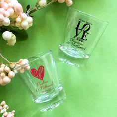 two shot glasses sitting next to each other on a green surface with flowers in the background