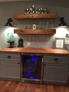 a wine cooler in the middle of a kitchen with shelves above it and glasses on top