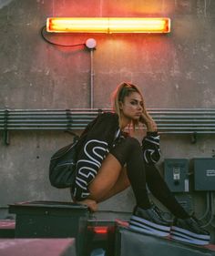 a woman sitting on top of a pile of luggage next to a neon light sign