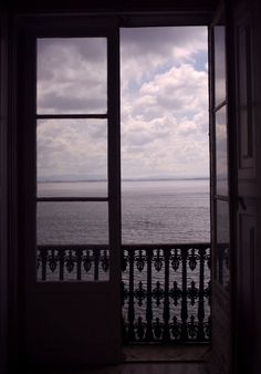 an open door leading to the ocean with clouds in the sky and water behind it