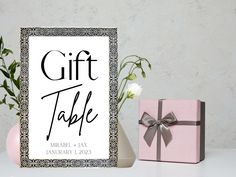 a gift table sign next to a pink vase with white flowers and a present box