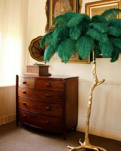 a tall palm tree sitting on top of a wooden dresser next to a painting and mirror