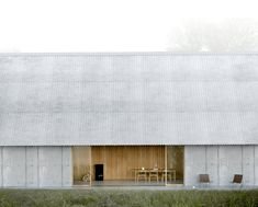 a white barn with two chairs and a table in front of it on the grass