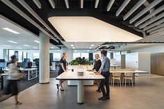 two people are standing at a table in an office setting with chairs and desks