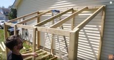 a man standing next to a house with wooden framing on it's sides and the roof being built