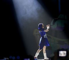 a woman in a blue dress and white boots is on stage with her arms outstretched