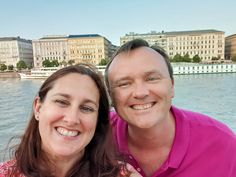 a man and woman posing for a picture in front of some buildings on the water