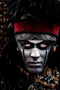 a man in black and white face paint with feathers on his head