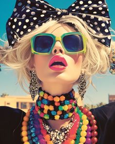 a woman wearing sunglasses and a bow tie with colorful beads on her neck, in front of a blue sky