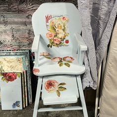 a white chair with flowers painted on it next to some books and other items in front of a wall