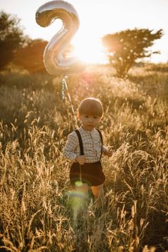 a little boy standing in tall grass with a number 2 balloon attached to his back