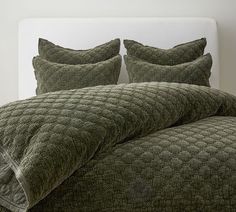 a bed with green comforter and pillows on it's headboard in front of a white wall