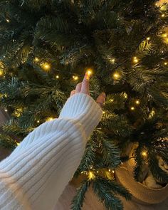 a person's hand in front of a christmas tree with lights on the branches