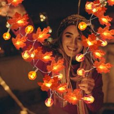 a woman is smiling and holding up some lights in the shape of leaves on her head