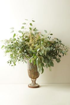 a vase filled with lots of greenery on top of a table