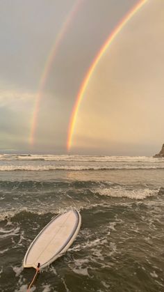 a surfboard in the water with a rainbow in the background