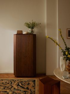 a vase with flowers on top of a wooden cabinet next to a rug and table