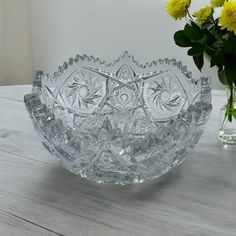 a glass bowl sitting on top of a wooden table next to a vase with yellow flowers