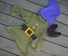 a green and blue outfit laying on top of a wooden floor next to a purple hat