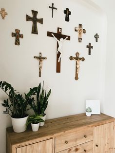 a wooden dresser topped with lots of crosses on the wall next to a potted plant