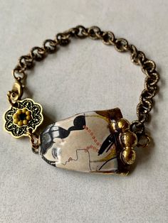 Art Deco inspired bracelet featuring a ceramic connector with a female image linked to a gold-plated brass floral connector with black and gold glass inlay. Bracelet fastens with a parrot clasp and bracelet measures 19cm in length. Handmade Artsy Gold Bracelets, Artsy Adjustable Gold Bracelet, Artsy Adjustable Gold Bracelets, Adjustable Artsy Gold Bracelet, Art Deco Handmade Bracelets As Gift, Adjustable Art Deco Jewelry Bracelet, Art Deco Metal Bracelets For Gifts, Art Deco Metal Bracelets Gift, Brass Art Deco Jewelry With Vintage Charm