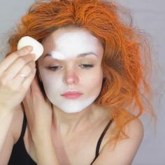 a woman with red hair is using a white mask on her face