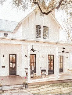 a white house with black doors and windows on the front porch is surrounded by trees