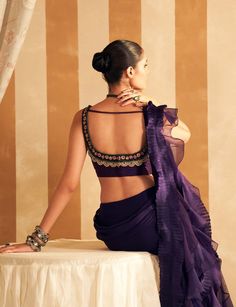 Enchant in the purple net embroidered sleeveless blouse paired with a chiffon organza double draped ruffle sari. The sleeveless blouse features intricate net embroidery in a regal purple hue, exuding sophistication. The sari, crafted from chiffon and organza, boasts a unique double draped ruffle design that flows gracefully, adding a touch of modern elegance. This ensemble beautifully blends classic charm with contemporary flair, perfect for any elegant occasion. Bollywood Evening Blouse With Ruffles, Organza Blouse With Traditional Drape, Sleeveless Pre-draped Saree With Intricate Embroidery, Elegant Purple Pre-draped Saree, Purple Organza Pre-draped Saree For Diwali, Elegant Sleeveless Organza Blouse, Purple Silk Pre-draped Saree For Party, Purple Silk Pre-draped Saree For Reception, Elegant Ruffled Blouse