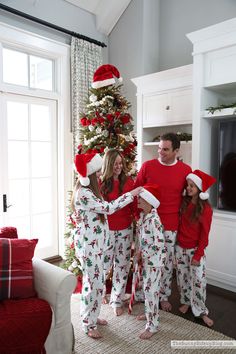 three people in matching christmas pajamas standing next to a christmas tree