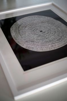 a white framed art piece with an intricate design in it's center, on a table