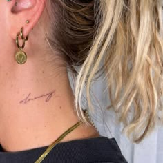 a woman with a small tattoo on her left side behind her ear is looking at the camera