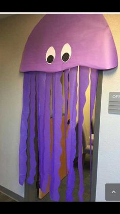 a purple jellyfish with googly eyes on it's head hanging from a wall