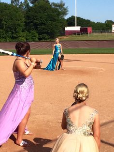 two girls in dresses are playing softball on a field with one girl holding a bat