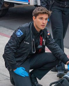 a man kneeling down next to a motorcycle on the side of the road while wearing blue gloves