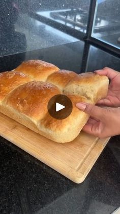 a person holding a loaf of bread on top of a wooden cutting board