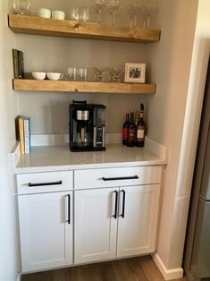 a kitchen with white cabinets and shelves filled with wine glasses, coffee maker and other items