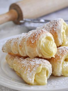 three pastries on a white plate with powdered sugar and a rolling pin in the background