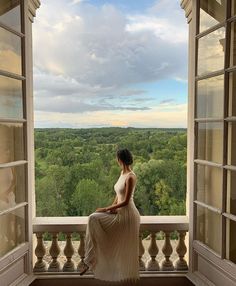 a woman sitting on a window sill looking out at the trees