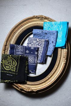 four different colored bandannas on a gold framed plate with black and blue napkins