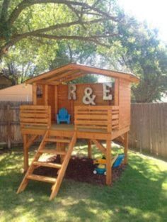 a wooden play structure with stairs and ladders in the grass next to a tree