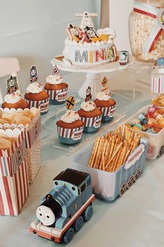 a table topped with cupcakes and cakes covered in frosting next to small train cars