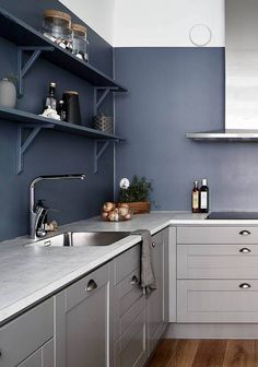 a kitchen with blue walls and white cabinets is pictured in this image, there are shelves on the wall above the sink