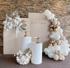 a table topped with white and gold balloons next to a greeting card, vases and candle holder