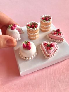 there is a miniature cake and heart shaped pastries on the plate that someone is holding