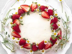 a cake decorated with strawberries and daisies on a white plate in the shape of a wreath