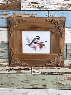 a bird sitting on top of a wooden frame with watercolors in the background