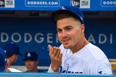 a baseball player sitting in the dugout with his hands clasped and other players standing behind him