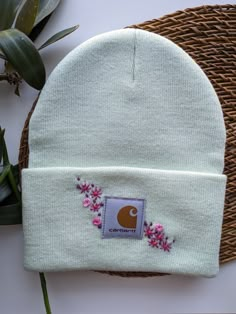 a white beanie with pink flowers on the side and a purple patch in the middle