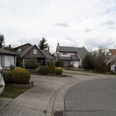 an empty street with houses and trees in the backround on a cloudy day