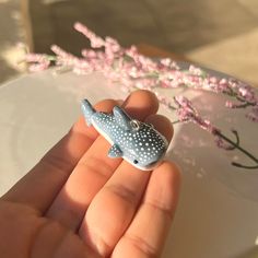 a hand holding a tiny toy whale in front of a flowered branch on a plate